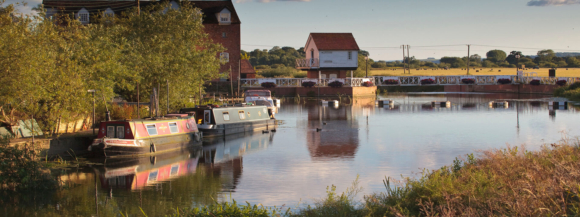 A riverside image with boats and houses in the background with reflections 
